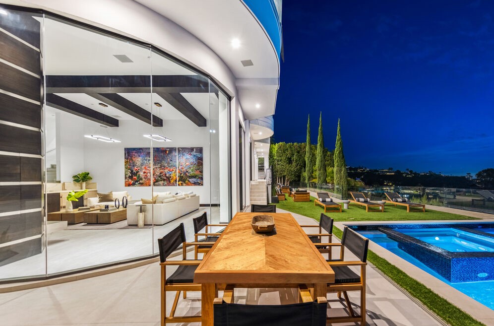 Twilight view of a hillside residence with retractable glass walls opening to a terrace, pool, and city lights beyond