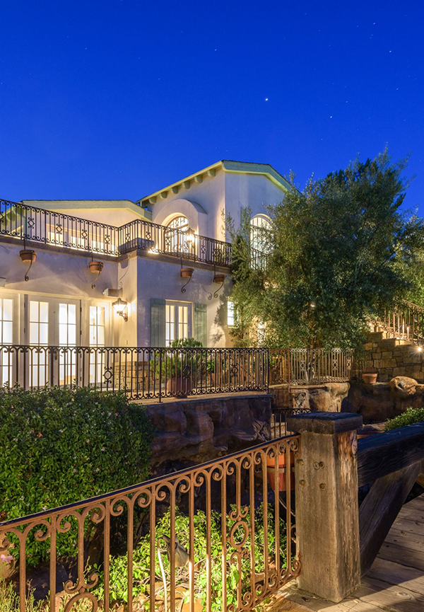 A Mediterranean-style hillside home at dusk with wrought-iron balconies and stone terracing